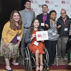 Staff and friends of IEL pose for a photo holding an "IEL at 50" poster.